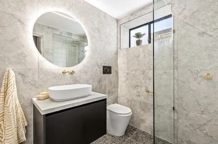 Renovated bathroom with round backlit mirror and stone look tiles, suited to an apartment renovation